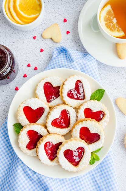 Linzerkoekjes met hart met frambozenjam en poedersuiker op een witte plaat met een kop thee.