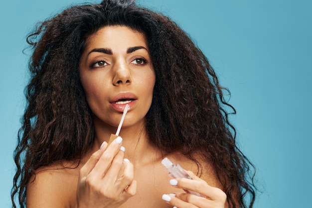 Lip augmentation concept pretty tanned curly latin woman
putting lipstick and looking aside over blue background free space
cosmetic lips product ad natural beauty makeup concept studio
portrait