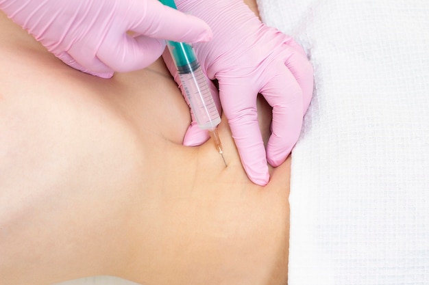 Lipolytic injections are placed in the stomach. female hands in pink gloves inject a young woman into the stomach.