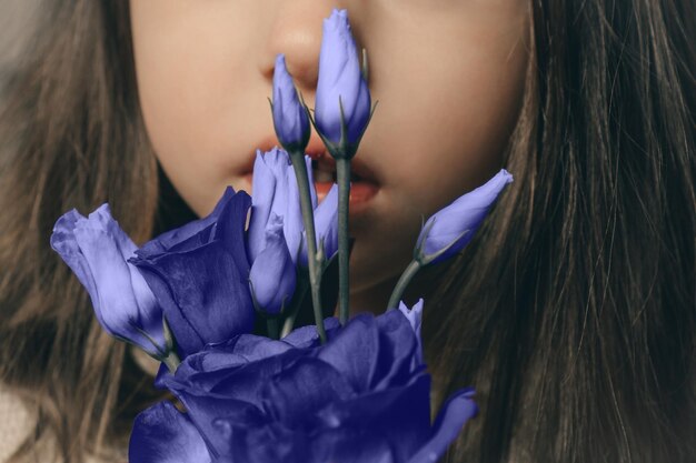 Lippen en wang van meisje naast Eustoma-bloemen van trendy kleur van het jaar 2022 Very Peri, modieuze paarse tint.