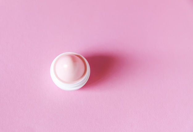 Lippenbalsem voor droge lippen in kleine witte plastic container op zachtroze achtergrond.