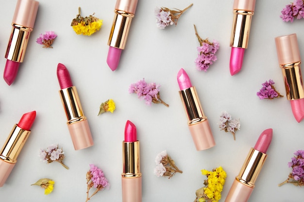 Lippenstift met mooie bloemen op grijze tafel. Bovenaanzicht