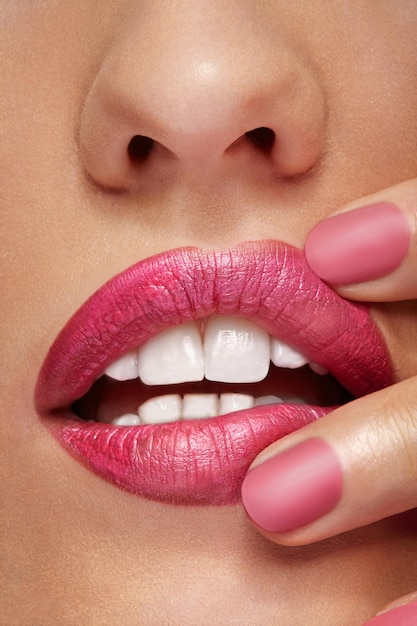 Lips with pink lipstick and fingers in photo in close up. Make up and lipstick