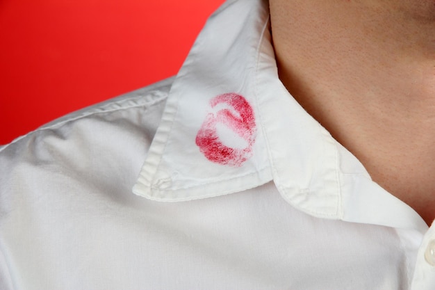 Lipstick kiss on shirt collar of man on red background