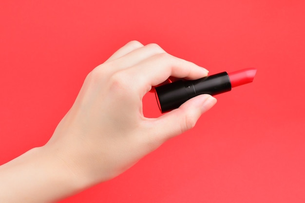 Rossetto in mano della donna isolata su fondo rosso.