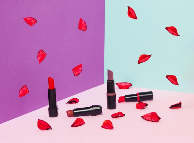 Lipsticks and red petals on colorful background Trendy make up background Beauty product concept