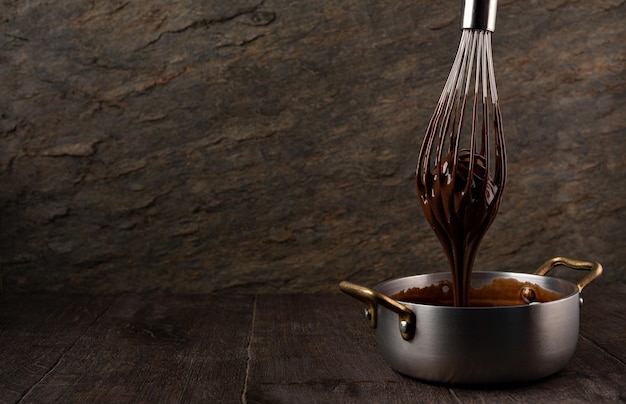 Liquid chocolate cream pouring from a whisk into a ladle