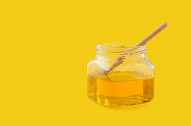 Liquid flower honey in glass jar with wooden honey spoon.