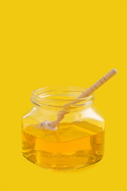 Liquid flower honey in glass jar with wooden honey spoon.