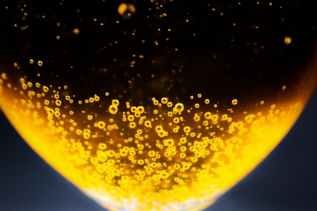 Liquid gold-yellow gasoline bubbles background on beer or champagne glass. Close up, macro shot. Soft focus photo.