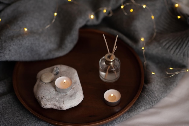 Liquid home fragrance with burning scented candle on stone tray over glow christmas lights at home close up Cozy hygge atmosphere with candlelight