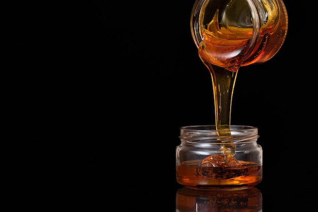 Liquid honey on a black background flows from one jar to another.