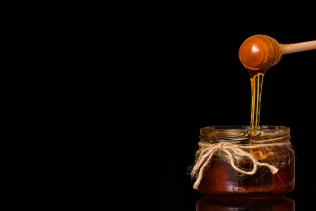 Liquid honey flows into a glass jar.