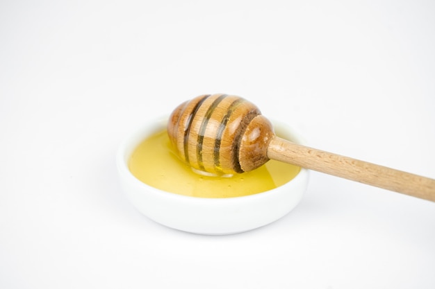 Liquid honey pouring with wooden stick in small white plate
