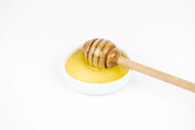 Liquid honey pouring with wooden stick in small white plate
