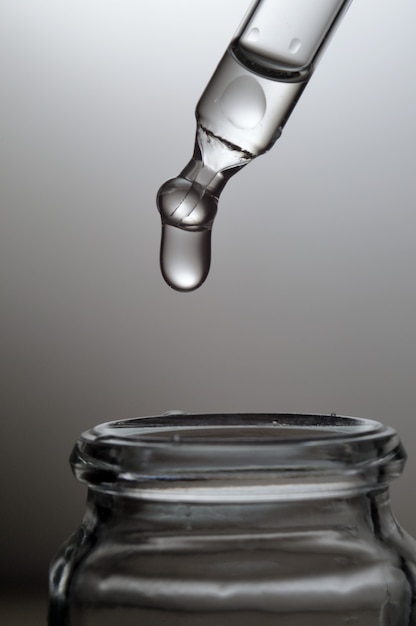 Liquid transparent gel or serum pipette with drops on gray background.