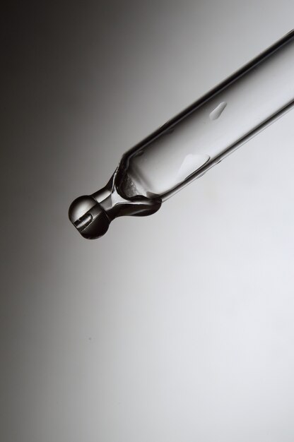 Liquid transparent gel or serum pipette with drops on gray background