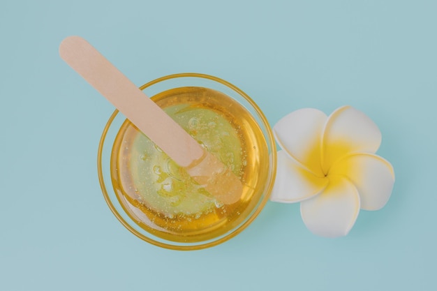 Liquid yellow sugar paste wooden spatula and flower on a blue background Removing unwanted hair