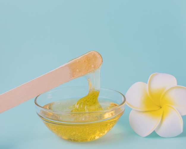 Liquid yellow sugar paste wooden spatula and flower on a blue background Removing unwanted hair