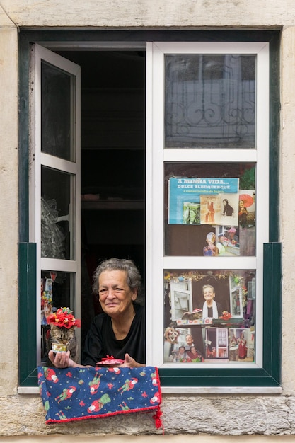 사진 포르투갈 리스본 100523 리스본의 유명한 노인 여성이 모자를 입은 고양이와 함께 창문에 앉아 있습니다.