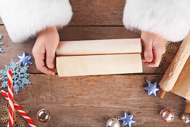 A list of Christmas wishes in Santa Claus hands on wooden table