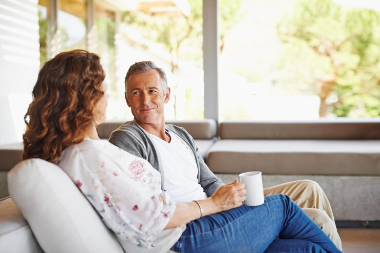 Photo listen coffee or mature couple in home living room for conversation or communication in marriage peace drinking tea or woman speaking to man in retirement house or discussion to relax together