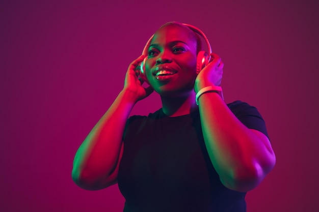 Listen to music. African-american young woman's portrait on purple background. Beautiful model in wireless headphones. Concept of emotions, facial expression, sales, ad, inclusion. Copyspace.