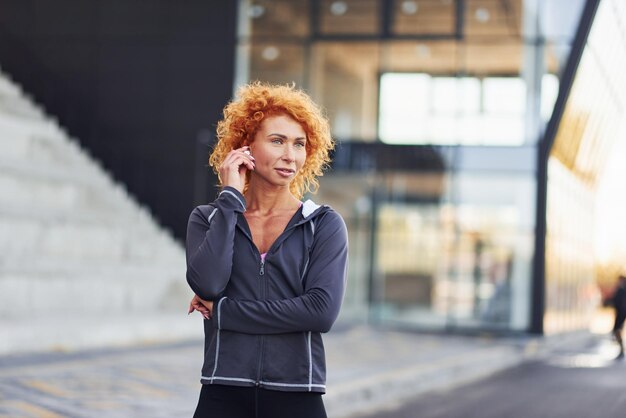 Listening to the music in headphones Portrait of young european redhead woman that standing outdoors