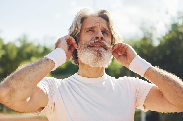 Listening to the music Senior modern stylish man outdoors on the sportive field at daytime