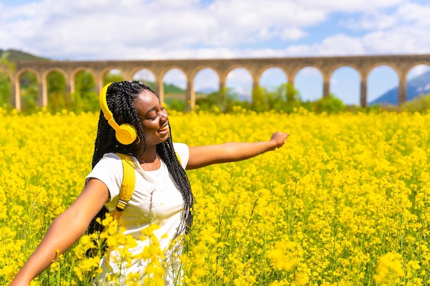 Listening to music in yellow headphones with closed eyes a black ethnic girl with braids a traveler in a field of yellow flowers