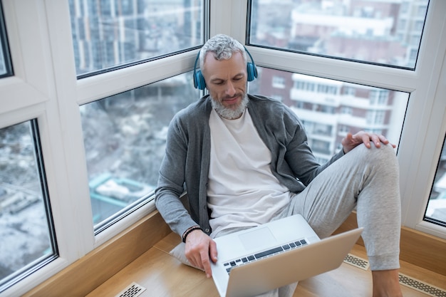 Listening something. A mature man with a laptop and in headphones listening to something on internet