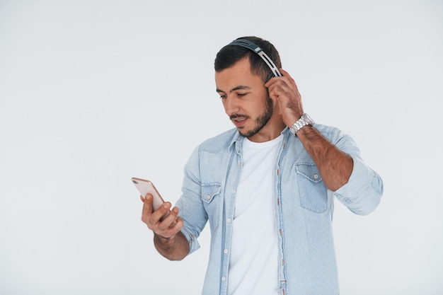 Listens to the music in headphones Young handsome man standing indoors against white background
