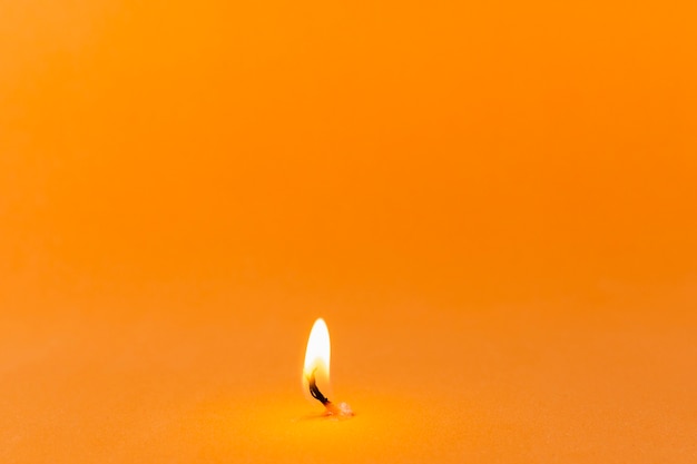Зажженная свеча на оранжевом фоне