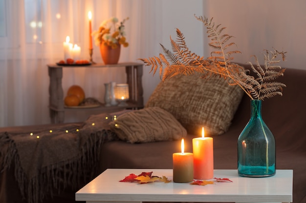 lit candles with autumn decor on white table at home