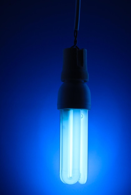 Photo a lit energy saving light bulb on blue background