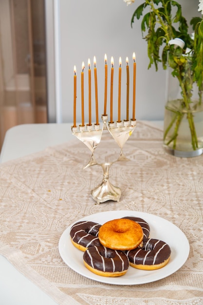 A lit Hanukkah with everyone on the festive table next to donuts and a vase of flowers. Vertical photo