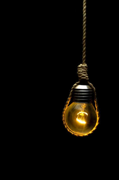 Photo lit light bulb hanging on a rope with black background