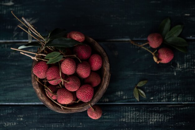 Litchi is placed in a wooden plate, peeled or unopened, on a dark wood grain table