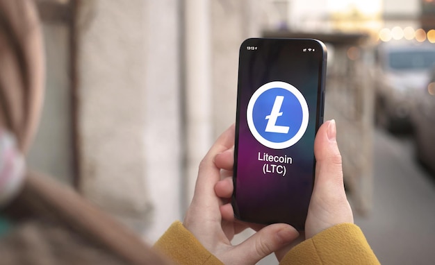 Символ криптовалюты Litecoin LTC, логотип. Бизнес и финансовая концепция. Рука со смартфоном, экран с крупным планом значок крипто