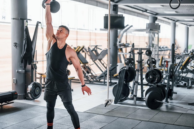 Peso leggero il giovane uomo sportivo e forte in abbigliamento nero ha una giornata di allenamento in palestra