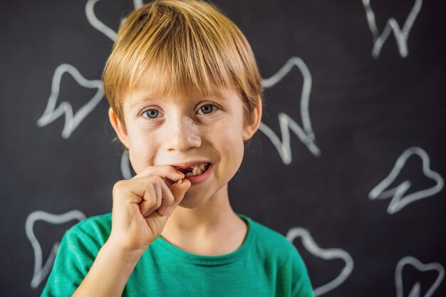 Photo litle caucasian boy holds a dropped milk tooth between his fingers and laughs looking into the camera