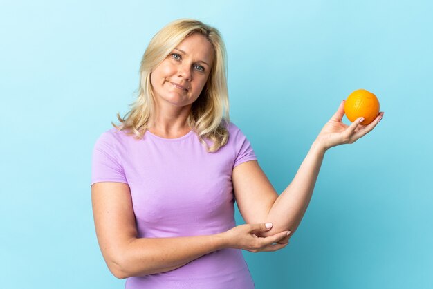 Litouwse vrouw van middelbare leeftijd die op blauwe muur wordt geïsoleerd die een sinaasappel houdt