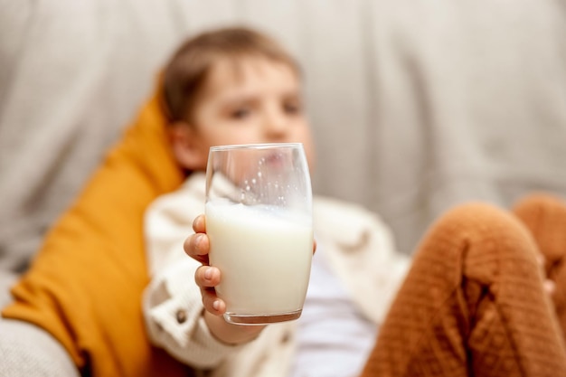 Photo little adorable boy sitting on the couch at home and drinking milk fresh milk in glass