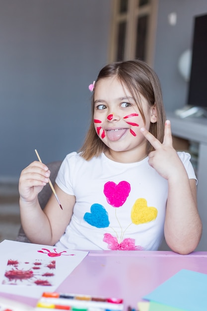 Little adorable cute cheerful joyful girl drawing alone at home during vacation or quarantine witn mouse on her face. Childhood home activity at home, art for kids