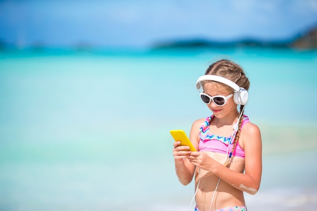 Little adorable girl listening music on the beach