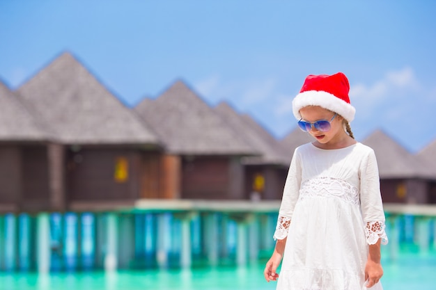 Piccola ragazza adorabile in cappello rosso di santa sulla spiaggia