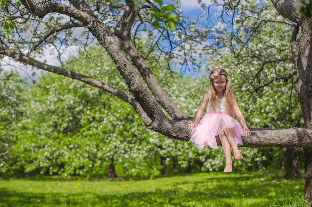 Little adorable girl sitting on blossoming apple tree