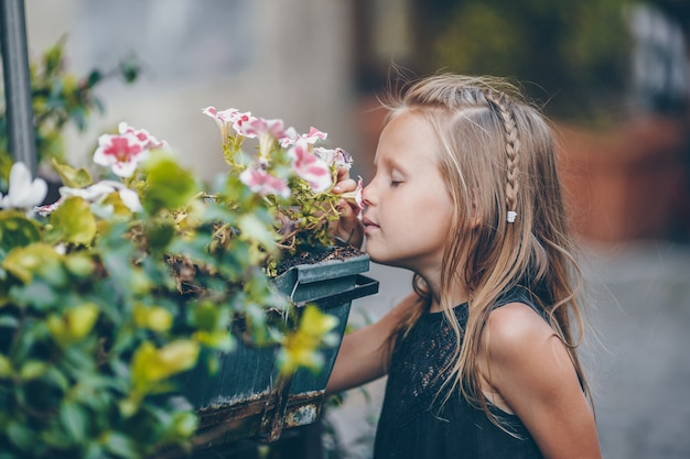 Little adorable girl sitting near colorful flowers in the garden
