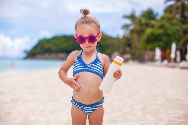 Foto la piccola ragazza adorabile in costume da bagno si strofina la protezione solare