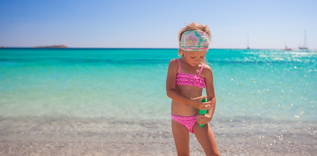 Little adorable girl in swimsuit with suntan lotion bottle